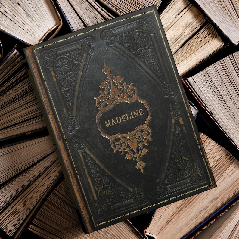 May include: A dark green book with gold accents and the name "MADELINE" in a gold frame. The book is surrounded by other books with open pages, creating a vintage aesthetic. The cover has an embossed design.
