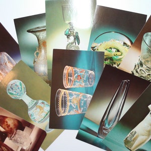 Puede incluir: Una colección de postales antiguas que muestran diversas piezas de arte en vidrio, incluyendo jarrones, cuencos y esculturas. Las postales están dispuestas en forma de abanico, con las imágenes mirando hacia afuera. Las postales están impresas en una variedad de colores, incluyendo azul, verde y dorado.