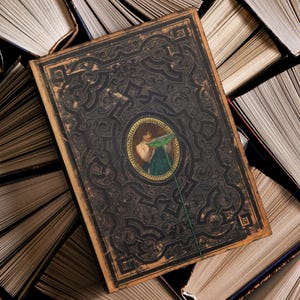 Pu&ograve; includere: Un libro d'epoca con una copertina scura con un design in rilievo e un ritratto ovale centrale. Il ritratto raffigura una donna che tiene in mano un oggetto verde. Il libro &egrave; circondato da altri libri aperti.