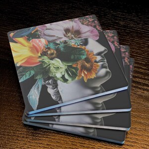 Puede incluir: Un juego de cuatro posavasos con un collage de la cara de una mujer con una corona de flores. Las flores son vibrantes y coloridas, incluyendo girasoles, flores rosas y blancas y hojas verdes. El fondo es negro.