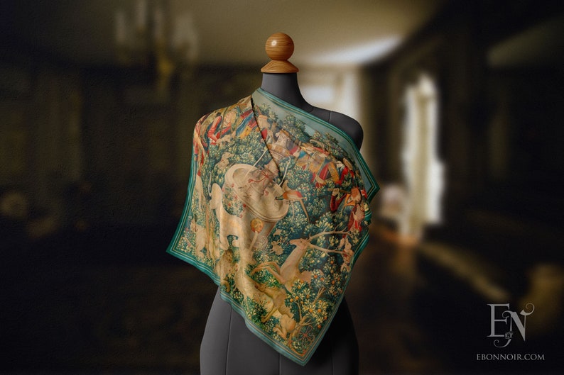 May include: A green silk scarf featuring a tapestry print of a unicorn hunt. The print depicts a white unicorn, a group of hunters, and a forest scene.