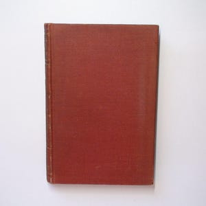 May include: A vintage book with a textured, reddish-brown cover. The spine shows signs of wear, suggesting age. The book is rectangular and appears to be closed, with a simple, classic design. The background is plain white.