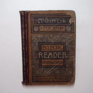 May include: An antique book titled "McGuffey's Fourth Eclectic Reader, Revised Edition." The cover is brown with black and gold lettering and decorative patterns. The book's spine is a darker brown.