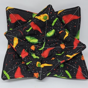 May include: Set of three black quilted hot pads with a chili pepper print. The hot pads are shaped like a star and have white stitching around the edges.