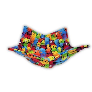 May include: A fabric bowl cozy featuring a vibrant, multi-colored pattern of cartoon dogs in shades of red, yellow, green, and blue. The square-shaped textile holder has four pointed corners and is constructed with visible stitching throughout.