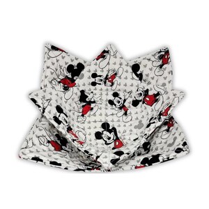 May include: A quilted fabric bowl cozy featuring a repeating pattern of Mickey Mouse in black, white, and red. The bowl cozy has a square base with four pointed, folded corners and visible stitching throughout the white fabric material.