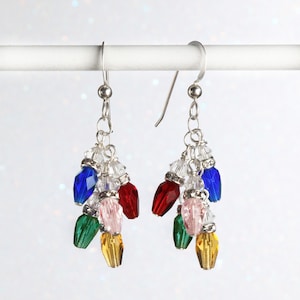 May include: Silver dangle earrings with a cluster of colorful crystal beads in the shape of Christmas lights. The beads are red, blue, green, pink, and yellow.