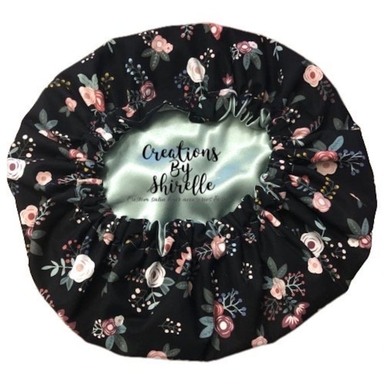 May include: Black satin bonnet with a floral print and a light blue satin lining. The bonnet has the text "Creations By Shirrelle" printed on the lining.