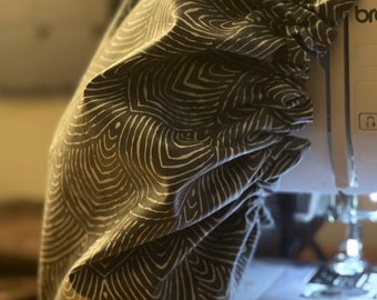 May include: A black and white patterned fabric sewing machine cover. The cover is made of a soft, stretchy fabric and has a drawstring closure. The cover is being sprayed with water.