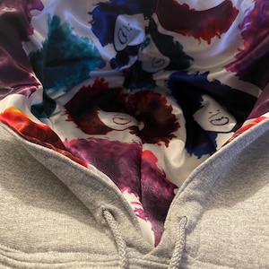 May include: Gray hooded sweatshirt with a white satin lining featuring a colorful abstract design. The lining has a watercolor effect with purple, blue, and green hues.