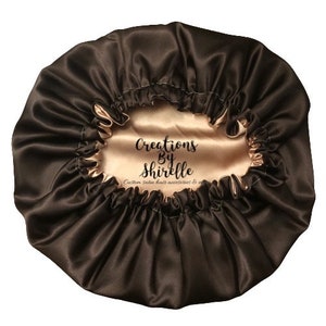 May include: A brown satin hair bonnet with a peach-colored satin lining. The bonnet has the text "Creations by Shirrelle" printed on the lining.