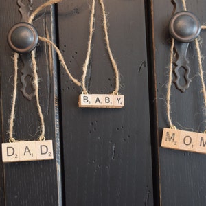 May include: Three wooden letter tiles spelling out "DAD", "MOM", and "BABY" hanging from twine on black cabinet doors.