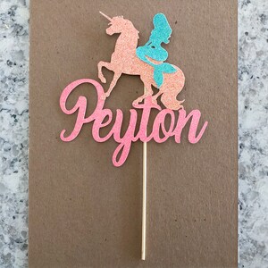 May include: Pink glitter cake topper with a mermaid riding a unicorn and the name Peyton.