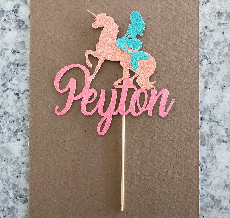 May include: Pink glitter cake topper with a mermaid riding a unicorn and the name Peyton.