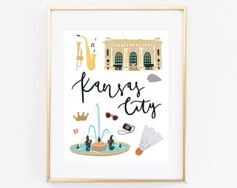 May include: A white background with a gold frame around a print of a city scene. The print features a yellow saxophone, a building with a green roof, a fountain, sunglasses, a camera, a badminton shuttlecock, and the text "Kansas City".