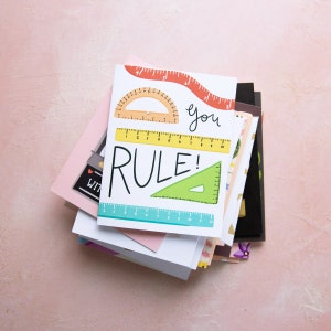 May include: A stack of colorful greeting cards with a ruler, protractor, and the text "you rule!" on the top card.