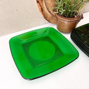 Può includere: Un piatto quadrato in vetro verde con un design a cerchio concentrico rialzato al centro. Il piatto è in vetro verde scuro e ha una finitura lucida.