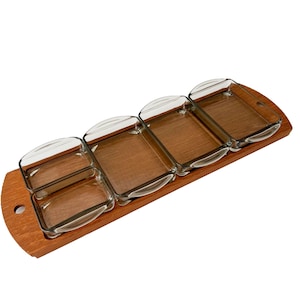 May include: A wooden serving tray with five clear glass rectangular dishes. The tray is made of light brown wood and has a rounded handle on one end. The glass dishes are arranged in a row and are empty.
