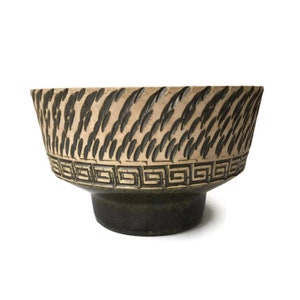 Puede incluir: Un cuenco de cerámica con un patrón geométrico marrón y negro. El cuenco tiene un borde ancho y una base estrecha.