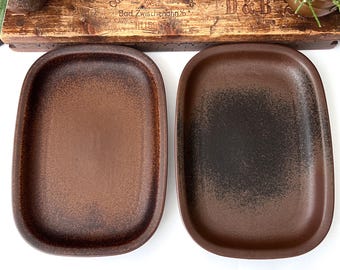 May include: Two rectangular brown ceramic serving platters with rounded corners. One platter has a solid brown color, while the other has a gradient effect, transitioning from brown to black. The platters are displayed on a white surface.