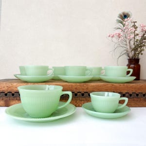 Puede incluir: Una taza de cerámica blanca con un asa negra y el texto "But First, Coffee" en un estilo manuscrito. La taza está sobre una superficie blanca. La taza mide aproximadamente 10 cm de alto.
