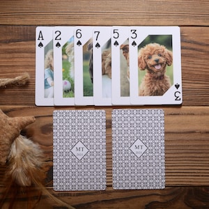 May include: Custom playing cards with photos of a child and dogs. The face cards show the Ace, 2, 6, 7, 5, and 3 of spades. The backs of the cards have a repeating geometric pattern with the initials "MT" and the year "2025".