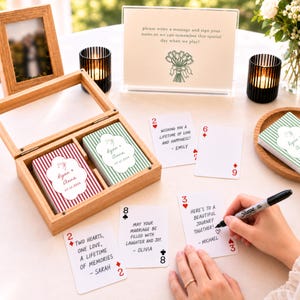 Könnte beinhalten: Eine Holzschachtel mit zwei Kartenspielen mit rot-grün gestreiften Rückseiten, personalisiert mit den Namen Ryan und Anna und dem Datum 07.12.2026. Mehrere Karten mit handschriftlichen Nachrichten liegen neben einem Schild mit Anweisungen.
