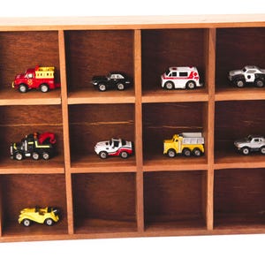 May include: A wooden display shelf with 12 compartments, each holding a miniature toy car or truck. The cars are in various colors, including red, yellow, white, and black.