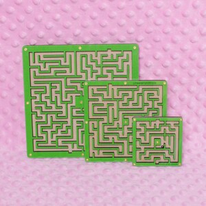 Three green plywood labyrinth mazes in small, medium, and large sizes against a soft pink background, showcasing a handmade maze game set.