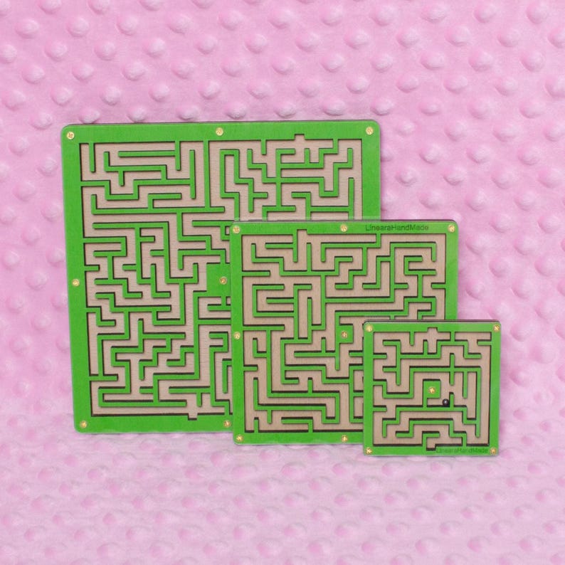 Three green plywood labyrinth mazes in small, medium, and large sizes against a soft pink background, showcasing a handmade maze game set.