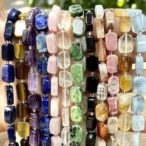 Puede incluir: Una colección de once pulseras de piedras preciosas multicolores dispuestas una al lado de la otra. Cada pulsera presenta cuentas rectangulares pulidas en varios colores, incluyendo azul profundo, marrón dorado, morado, rosa, transparente, verde, negro y azul claro.
