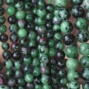 May include: A strand of green, black, and pink gemstone beads. The beads are round and have a speckled appearance.