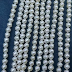 May include: Multiple vertical strands of lustrous, round white pearls arranged in parallel rows. Each individual pearl exhibits a smooth, reflective surface with a subtle iridescent sheen, creating a uniform and consistent appearance across all strands.