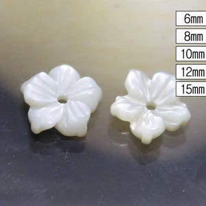 Op de afbeelding: Twee witte parelmoer knopen in de vorm van een bloem met een gat in het midden. De knopen zijn 6 mm, 8 mm, 10 mm, 12 mm en 15 mm groot.