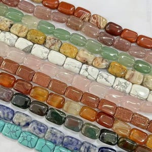 Puede incluir: Una colección de cuentas rectangulares de piedras preciosas dispuestas en filas paralelas, con una variedad de colores que incluyen turquesa, azul, negro, marrón, naranja, blanco y verde, con algunas cuentas que muestran patrones veteados y otras texturas brillantes.