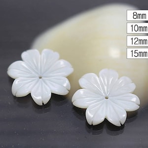 May include: Two white shell flower-shaped buttons with a carved design. The buttons are 8mm, 10mm, 12mm, and 15mm in size.