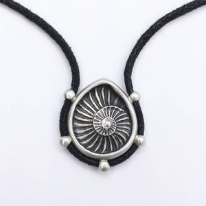 May include: A silver pendant necklace with a spiral design, hanging from a black cord.