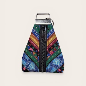 May include: A colorful, triangular keychain pouch with a black zipper. The pouch features a vibrant pattern of blue, green, red, and gold geometric shapes and designs. A silver-colored metal loop is attached at the top.