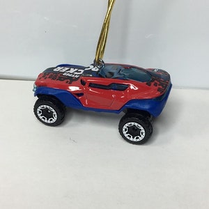 May include: A red and blue toy car with black wheels and a gold string for hanging. The car has the word "HYPER" printed on the top. The toy car is a miniature replica of a larger vehicle.