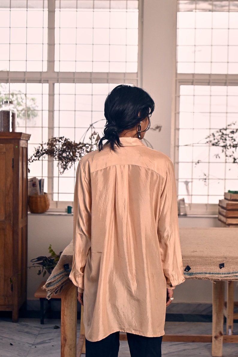 May include: A long-sleeved, peach-colored silk shirt with a collared neckline and button closure. The shirt is loose-fitting and has a relaxed silhouette.