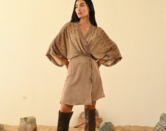Peut inclure: Une femme portant une robe portefeuille marron à imprimé floral et des bottes hautes en cuir marron. Elle se tient dans un décor désertique avec des rochers éparpillés autour d'elle.