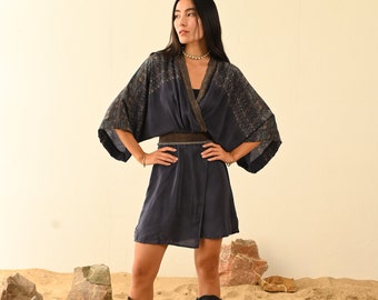 Peut inclure: Une femme portant une robe bleu foncé de style kimono avec un motif. Elle se tient sur une surface sablonneuse avec des rochers autour d'elle. Elle porte des bottes noires.