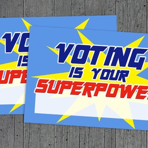May include: Two blue and yellow signs with the text "Voting is your superpower" in a comic book style font. The signs are blank and ready to be filled in.
