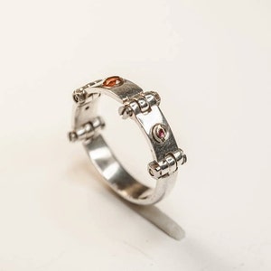 May include: A silver ring with a unique design featuring small, round, red and orange gemstones set into the band.