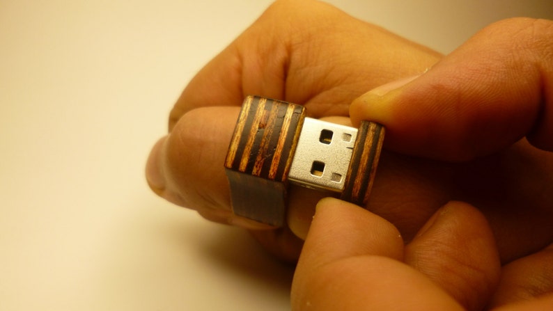 Op de afbeelding: Een houten USB-stick met een gestreept patroon. De stick is open, waardoor de zilveren USB-connector zichtbaar is.