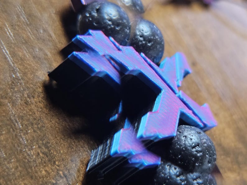 May include: Close-up of a blue and purple X-shaped object with a layered design, resting on a wooden surface. The object is paired with several dark, spherical, textured stones.