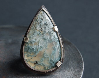 May include: A teardrop-shaped ring with a silver setting and a green and white agate stone.