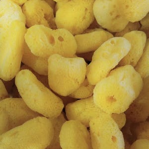 Puede incluir: Primer plano de un cuenco lleno de esponjas de baño amarillas. Las esponjas son de varias formas y tamaños, y algunas tienen una superficie texturizada.