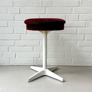 May include: A white adjustable stool with a burgundy plush seat. The stool has a star-shaped base.