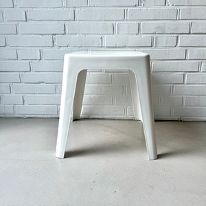 May include: A white plastic stool with a simple, modern design. The stool has a square top and four legs.